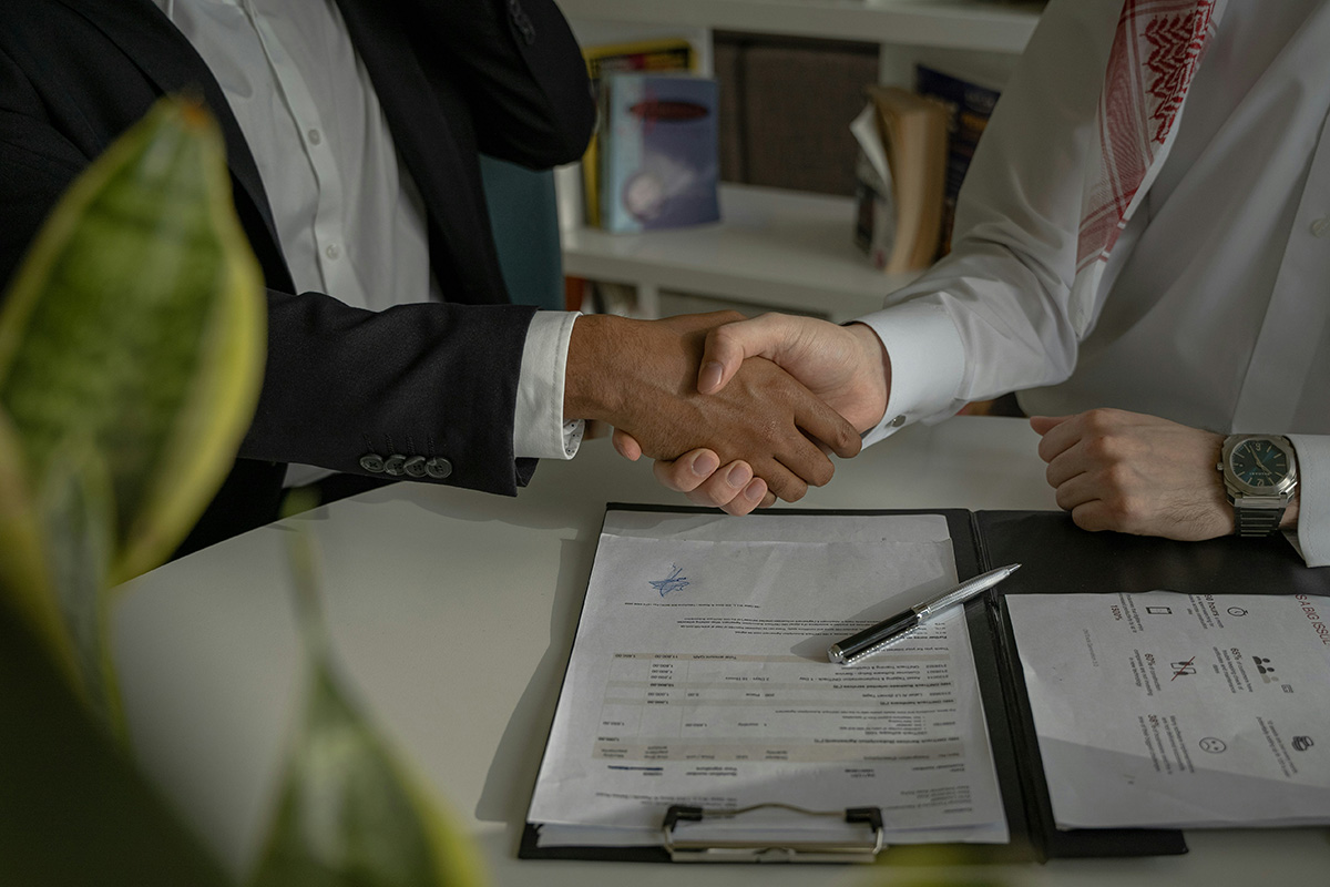 Generic negotiation graphic of two people shaking hands over documents. 